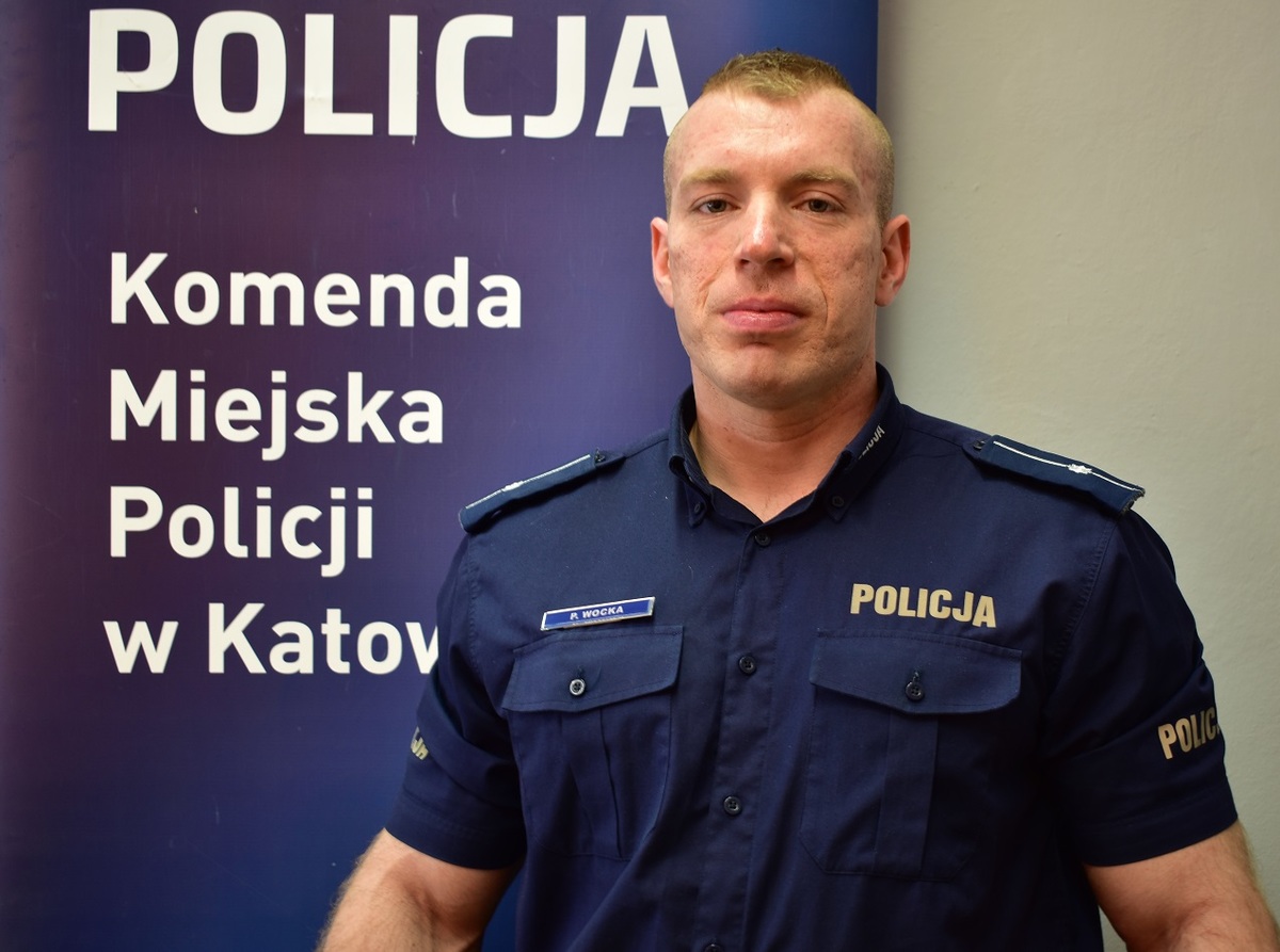 młodszy aspirant piotr wocka z komendy miejskiej policji w katowicach stoi na tle logo policji w katowicach