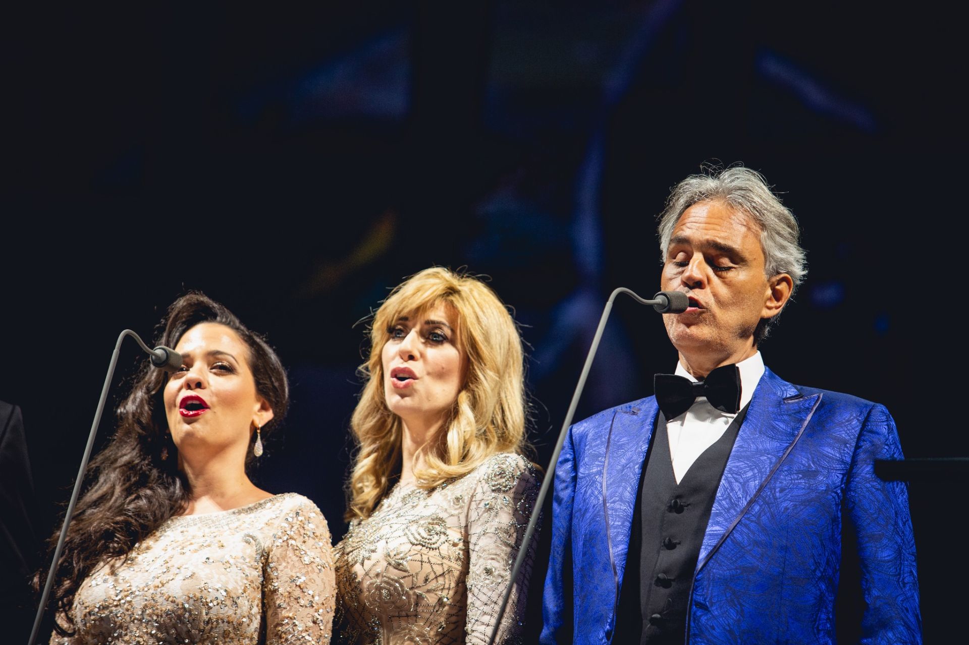 Andrei Bocelli i dwie śpiewaczki na czarnym tle
