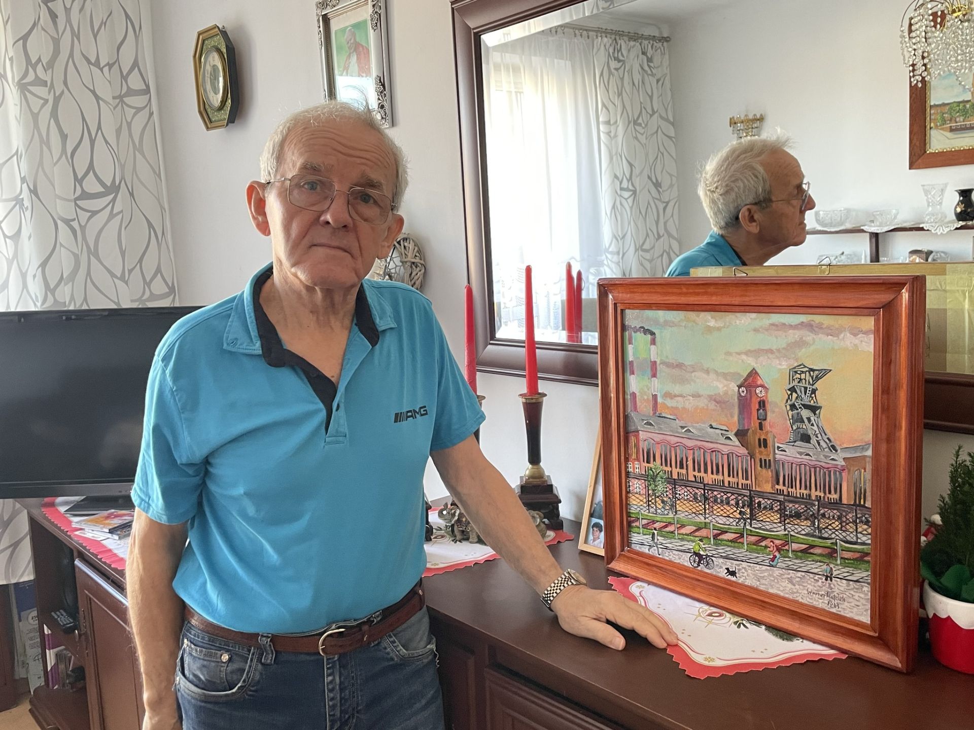 senior w niebieskiej koszuli stoi do zdjęcia przy swoim obrazie